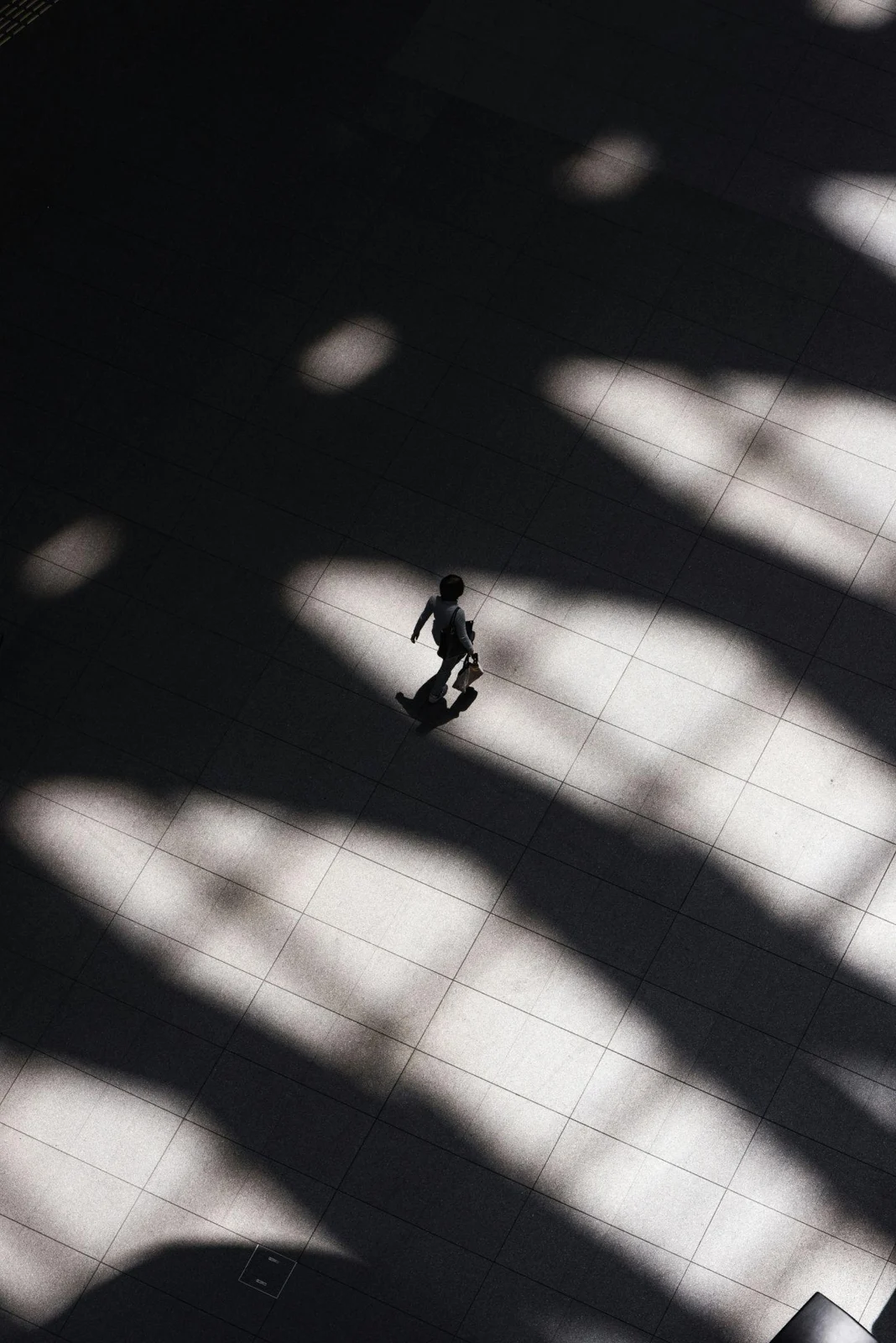 A solitary person crossing architectural shadows and a pool of light